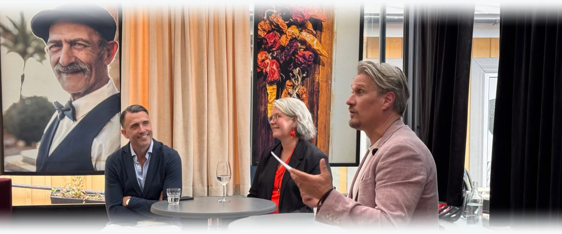 A panel conversation: three people at high tables, one of them speaking.